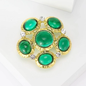 Detail of vintage gold brooch with hammered texture, green stones and white rhinestones