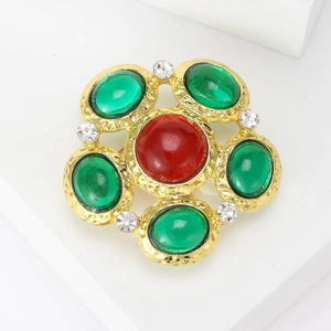 Detail of vintage round brooch with red and green glazed stones on golden frame