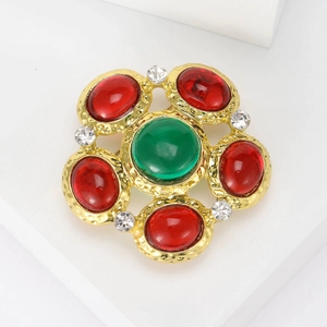 Macro detail of retro royal brooch with green and red gems on a gold textured base