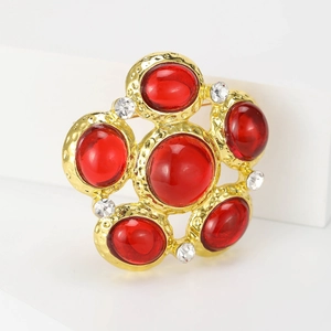 Detail view of retro flower brooch with red glass gems and gold hammered metal texture