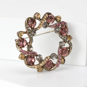 Broche couronne dorée vintage avec cristaux colorés sur un fond géométrique blanc