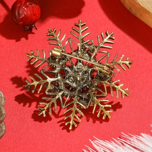 Vintage gold snowflake brooch with rhinestone details on a festive red holiday background