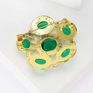 Vintage gold brooch with green glass stones featuring a secure back safety pin closure