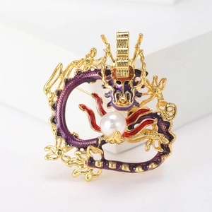 Golden dragon brooch with red and purple enamel and a white pearl on a white background