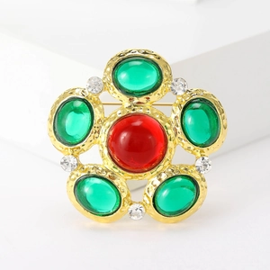 Vintage gold brooch with central red gemstone and surrounding green stones on white stand