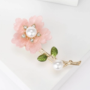 Detailed close-up of a pink cherry blossom brooch with white pearls and gold leaves