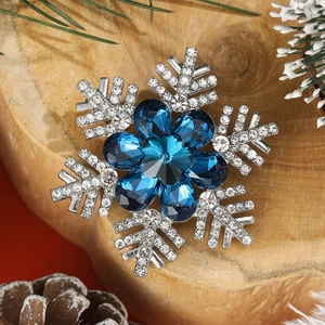 Detail einer silbernen Schneeflocken-Brosche mit blauen Steinen auf rustikalem Holzgrund