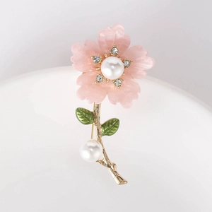 Detailed view of daisy brooch with pink petals, white pearls and green enamel leaves