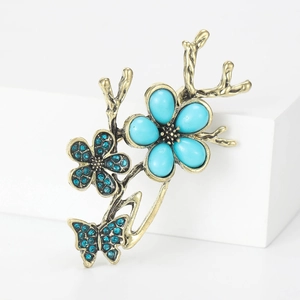 Elegant vintage butterfly and branch brooch with turquoise-toned gems on white cube stand