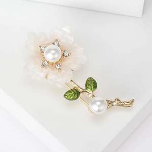 Detail of floral daisy brooch featuring white petals, pearl center and green enamel leaves