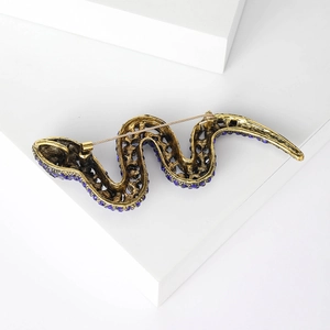 Vintage gold snake brooch with blue rhinestones and safety pin clasp on a white stone