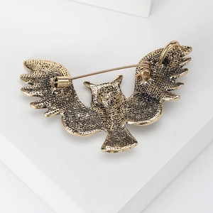 Vintage gold owl brooch with rhinestone wings and secure pin clasp on a white stand