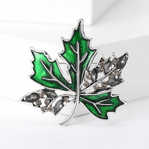 Détail de la broche feuille d'érable en émail vert et strass gris sur un bloc blanc
