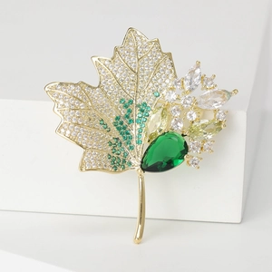 Detailed macro view of maple leaf brooch with green crystals and gold plating