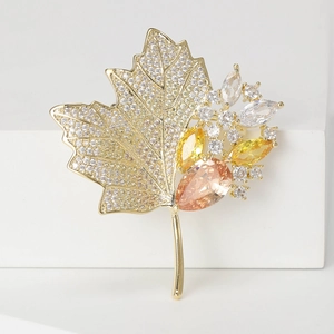 Elegant gold maple leaf brooch with sparkling crystals and amber gemstones on white surface
