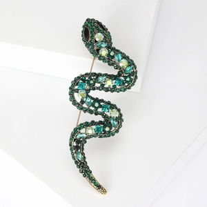 Elegant gold snake brooch with green rhinestones and crystals on white display stand