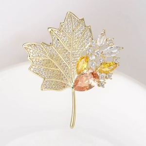 Macro view of gold maple leaf brooch with sparkling zircons and orange teardrop gem
