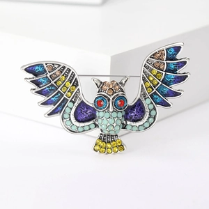 Macro detail of silver owl brooch with multi-color rhinestones on a white pedestal