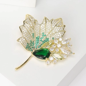 Macro detail of maple leaf brooch with green zircons and sparkling crystals on gold metal