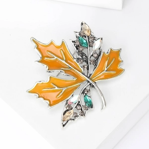 Détail macro d'une broche feuille d'érable en émail orange avec cristaux multicolores