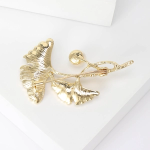 Elegante gouden ginkgoblad broche met parel en veiligheidssluiting op witte achtergrond