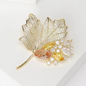 Detailed macro view of gold plated maple leaf brooch with sparkling zircons and amber gems