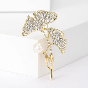 Detailopname van de gouden ginkgobladbroche met kristallen en een witte parel