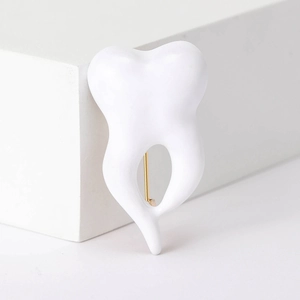 Detail view of a white crown tooth brooch with a polished gold metal pin back