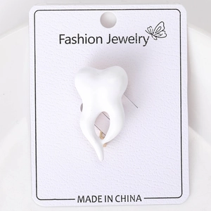 Close-up of a white enamel crown tooth brooch on a fashion jewelry display card