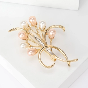Dettaglio di una spilla floreale dorata con perle bianche e rosa e piccoli cristalli