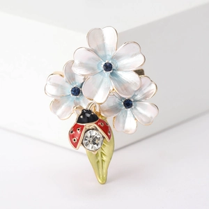 Gros plan d'une broche fleur et coccinelle émaillée avec cristaux bleus et feuille verte
