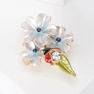 Détail d'une broche coccinelle sur fleurs bleues avec feuille verte et cristal