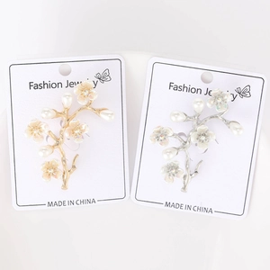 Dettaglio di eleganti spille a ramo di pesco con petali iridescenti e perle bianche