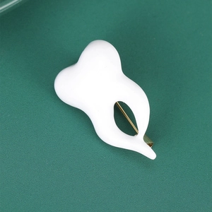 Macro shot of white resin crown tooth brooch with golden pin on dark green background
