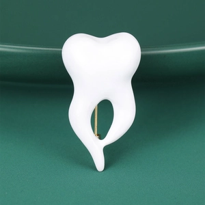 Detailed close-up of a white crown tooth enamel brooch with gold-tone pin on a green plate