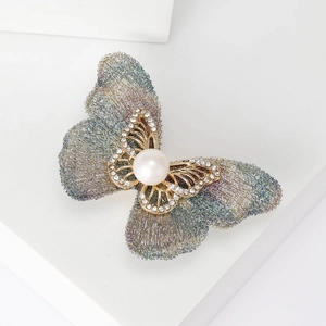 Détail d'une broche papillon en fil tissé avec cristaux brillants et perle blanche