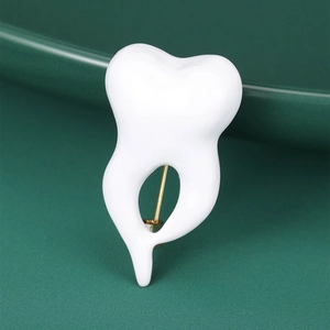 Detailed view of crown tooth brooch with glossy white oil drip finish on green background