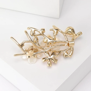 Elegant gold flower branch brooch with pearls displayed on a white geometric stand