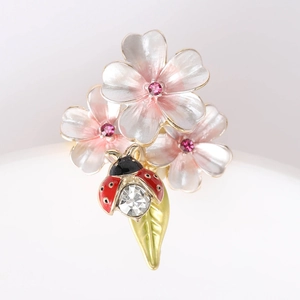 Détail macro d'une broche fleur en émail avec strass roses et épingle coccinelle en cristal