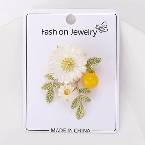 Vue détaillée d'une broche marguerite avec pétales en nacre et feuilles vertes mates