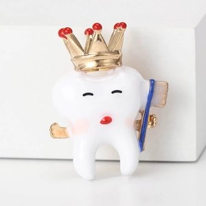 Creative tooth brooch with gold crown and blue toothbrush on a white display stand