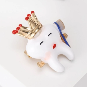 Detailed macro of a cute enamel tooth brooch with a golden crown and toothbrush accessory