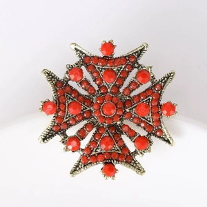 Détail macro d'une broche croix de Malte bohème avec pierres en résine rouge et or vieilli