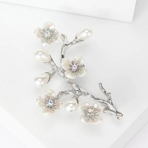 Dettaglio macro di un'elegante spilla a fiore argento con perle e strass su base bianca