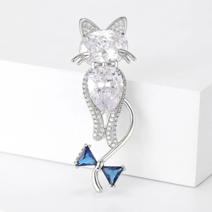 Sparkling cat brooch with white zircons and blue bow detail on white pedestal