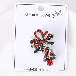 Macro-opname van een zilveren kerstbel-broche met rode en groene strass-steentjes op kaart