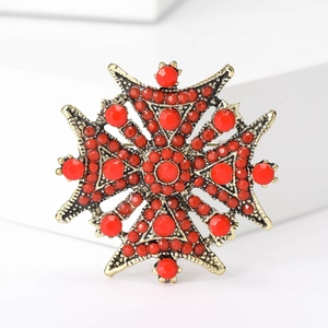Détail d'une broche croix héraldique vintage avec base dorée antique et perles rouges