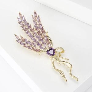 Macro detail of wheat brooch with purple zircons and golden ribbon tassel on white steps