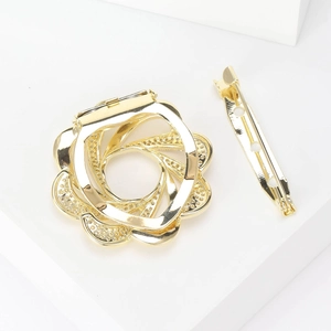 Broche fleur dorée aux pétales en spirale et zircons sur un socle géométrique blanc