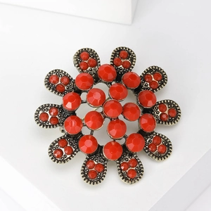 Détail macro d'une broche florale rétro en bronze avec pétales en résine rouge facettée